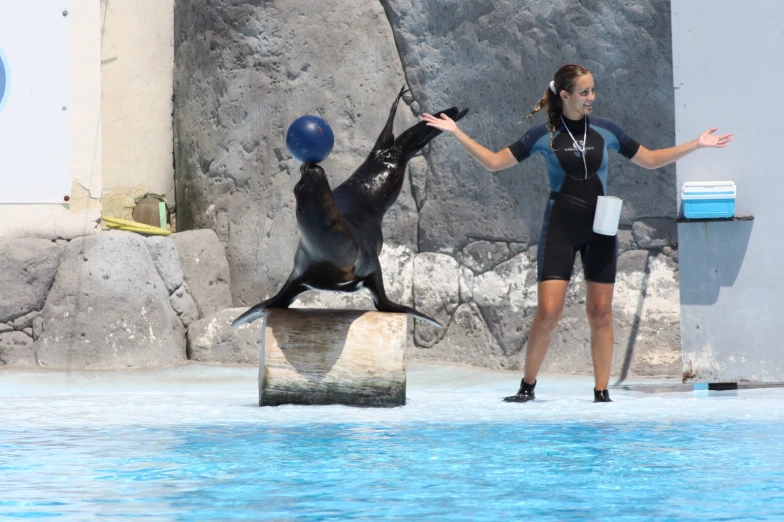 there is a female in a wet suit that is standing by a sea lion