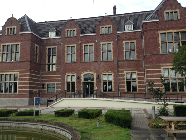 a brick building has an ornamental fountain and some bushes