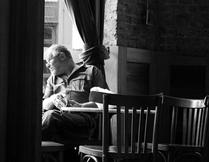 an old man sitting at a table, in front of a window