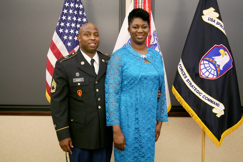 an officer and woman pose in front of american flags