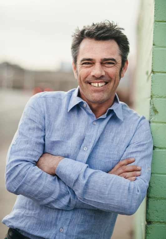 smiling man in blue shirt leaning against green wall