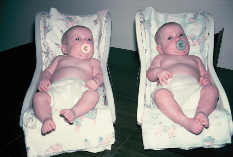 two identical babies in diapers sit on blankets