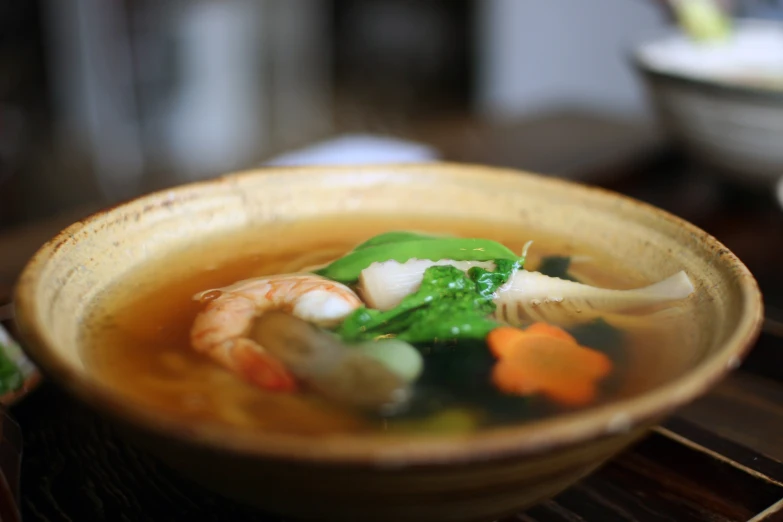 a bowl of soup with shrimp, broccoli, and carrots