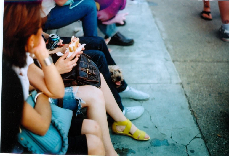 a group of women sitting on the side walk while eating food