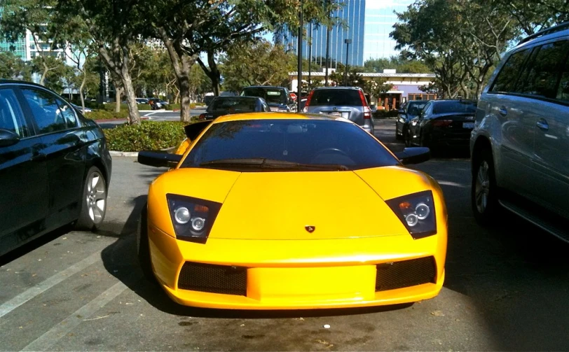 the yellow sports car is parked between two other vehicles