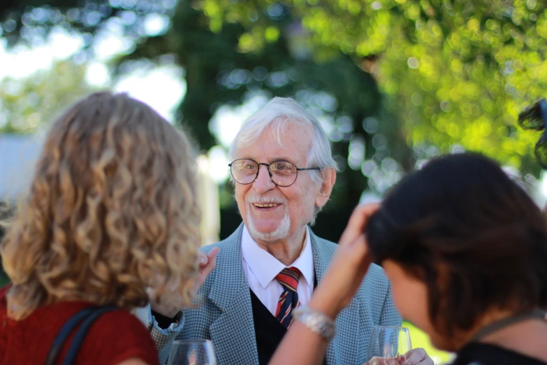 an older man with glasses and a tie talking to two women