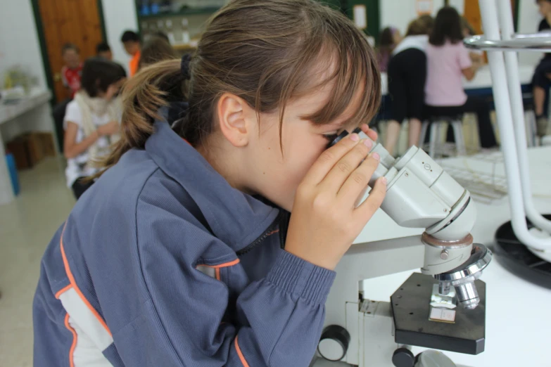 little girl looking through a microscope into the lens