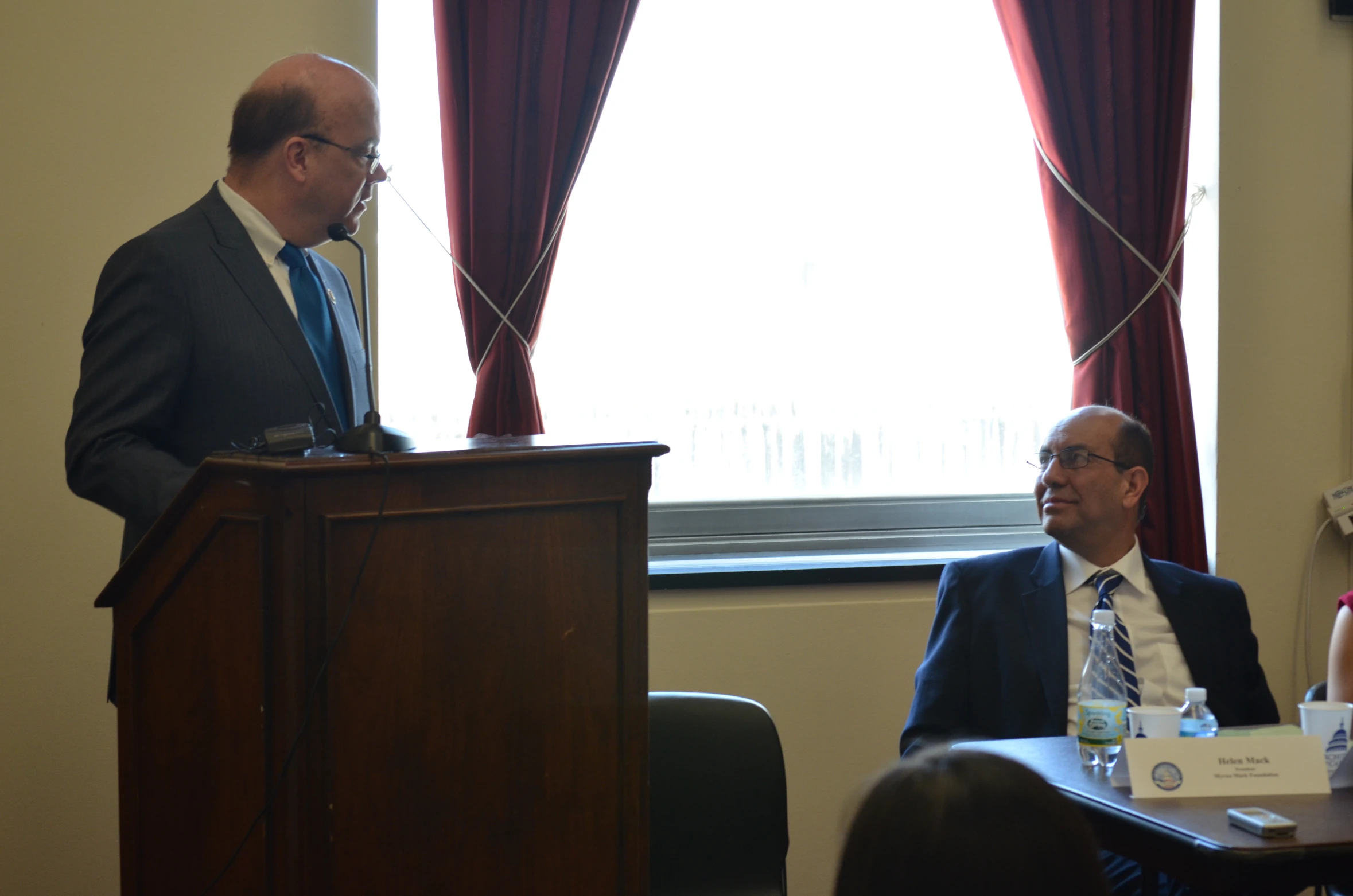 two men are standing at the podium of a conference room