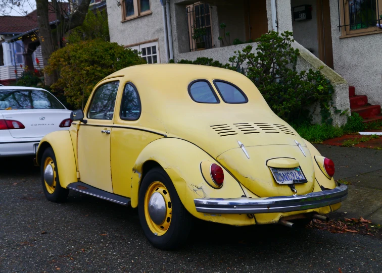 an old yellow vw bug sits outside of a house