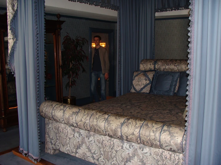 man in fancy bedspread, standing in doorway, in bedroom