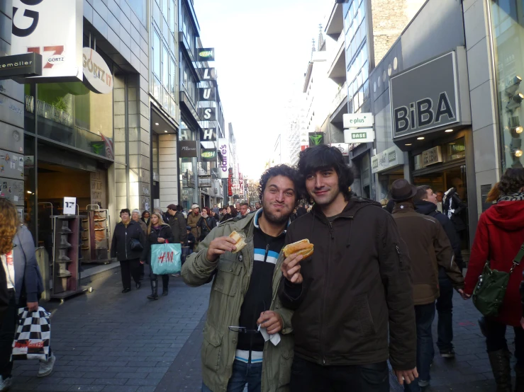 two young men are eating  dogs on a city street