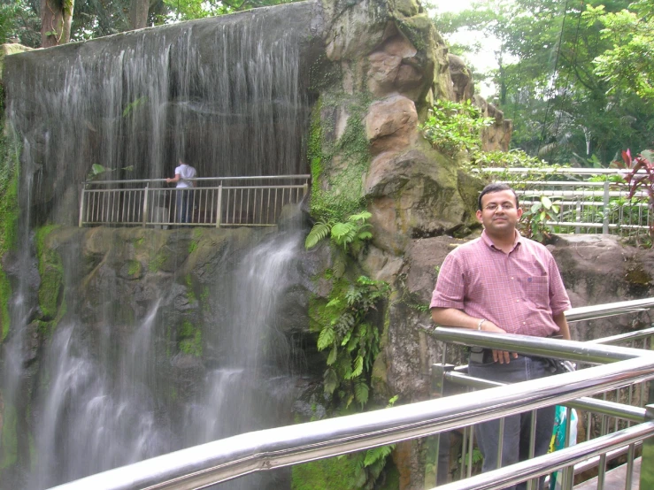 a man stands in front of a waterfall at the zoo