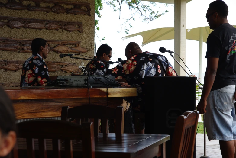 two males and one female in black hawaiian shirts are singing at an outdoor stand up mic