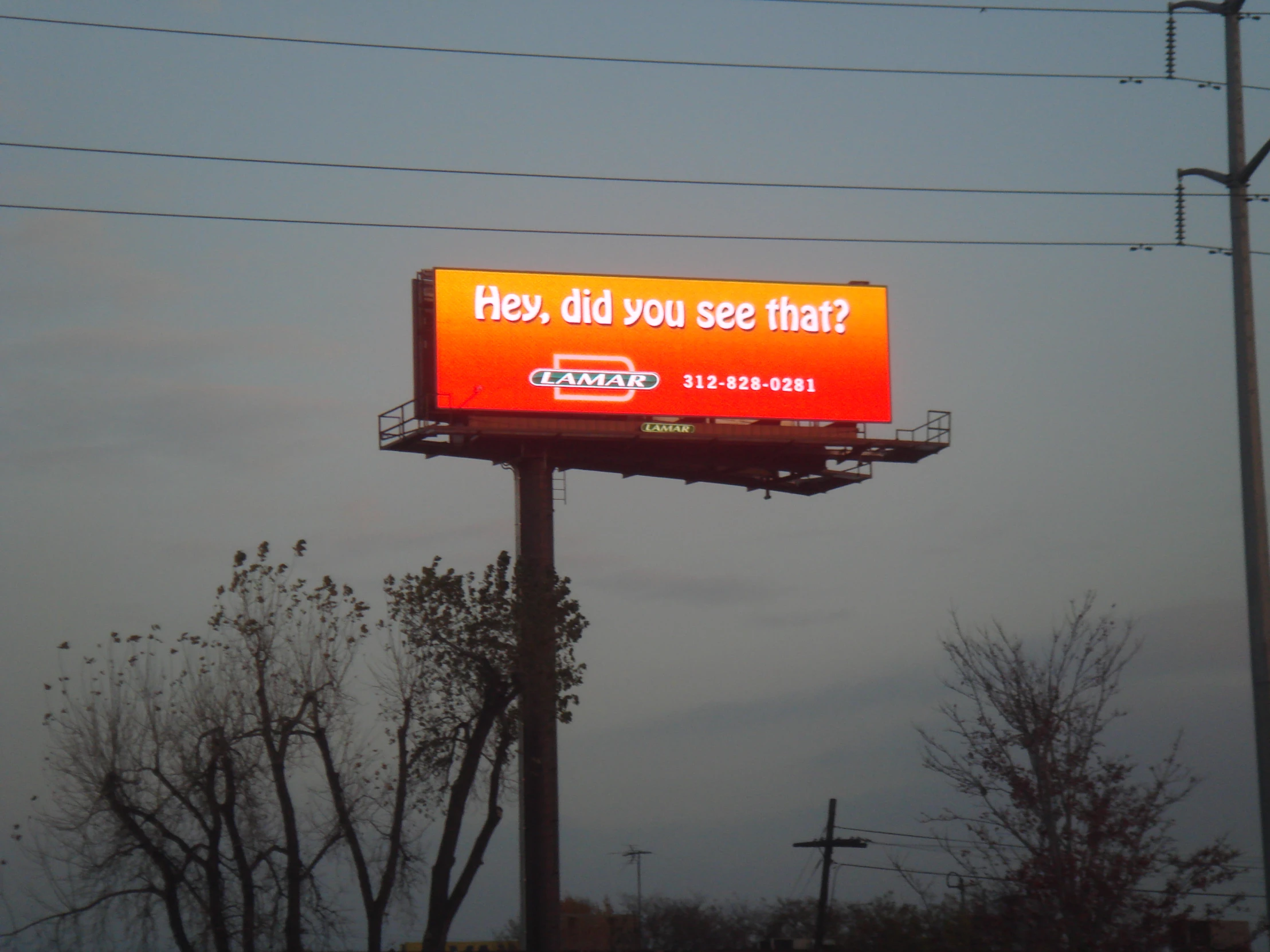 an orange and white sign and wires and trees