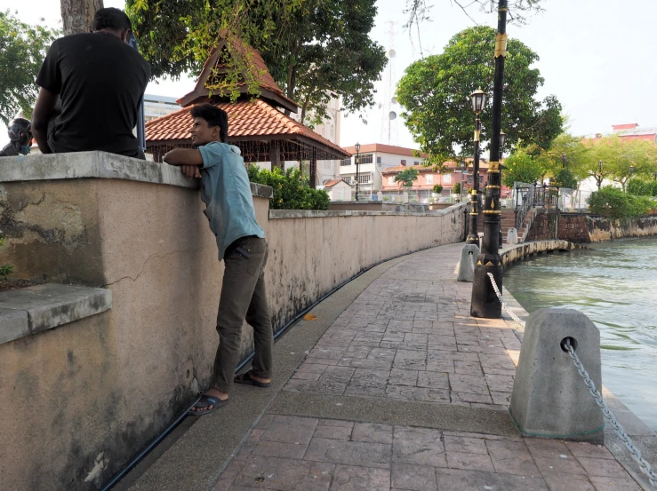 a man leaning up against a stone wall next to the water