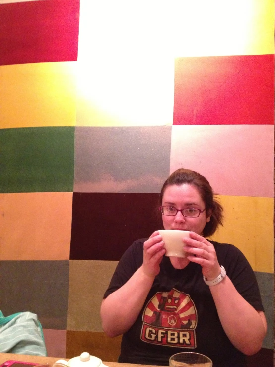 a woman is drinking a cup of coffee with a wall made out of multicolored squares