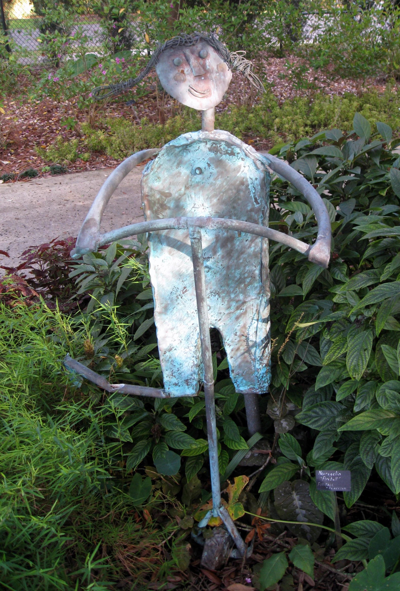 a rusty iron figure standing in the middle of a lush green garden