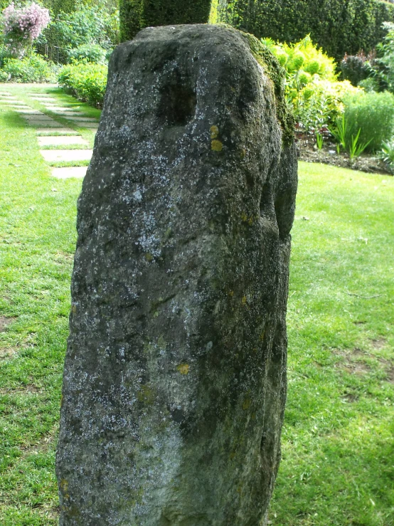 a rock standing in the grass with a walkway going around it