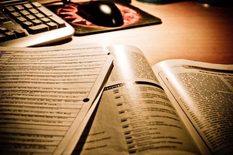 an open book sitting next to a keyboard on a wooden table