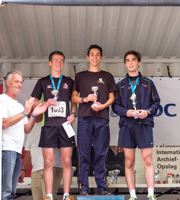 four men stand on a stage as one of them holds two medals