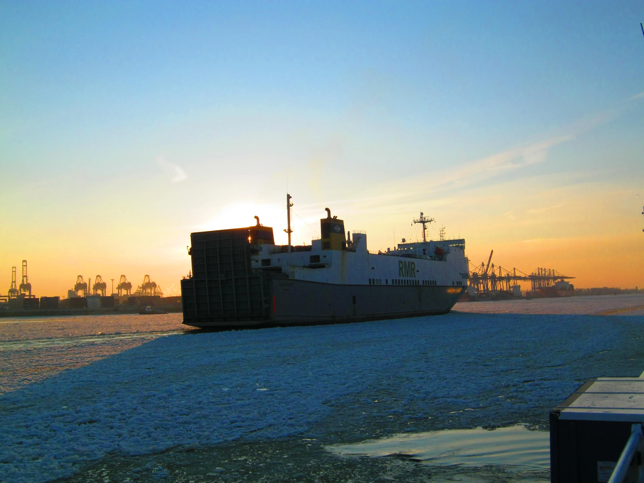 cargo ship in a harbor with cranes and ships in the background