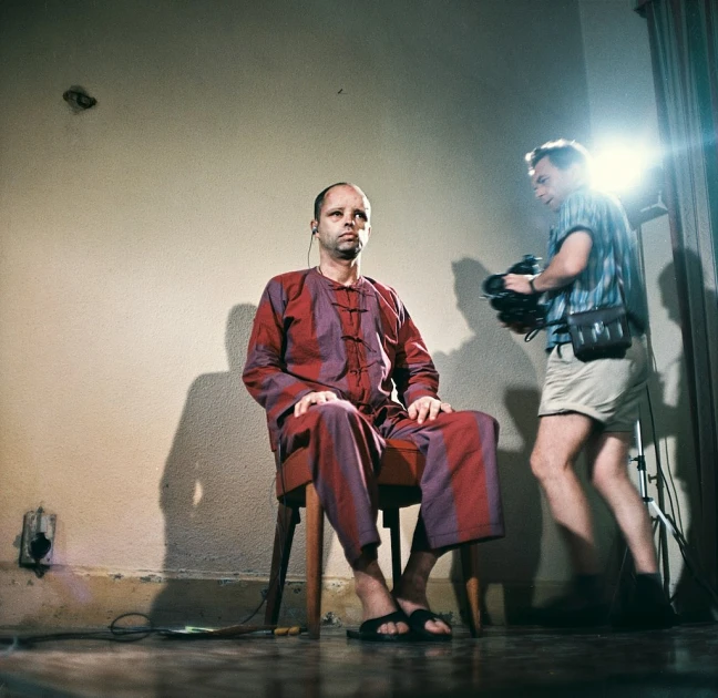 man sitting on chair looking into mirror with pographer behind him