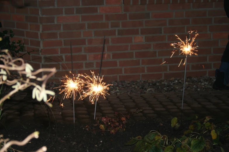 three sparklers near each other in front of a brick wall