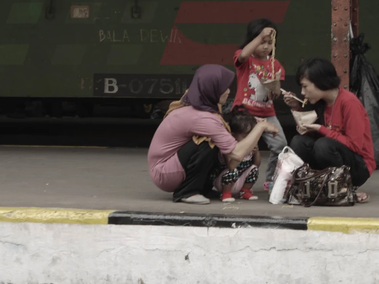 a group of people eating food sitting on the ground