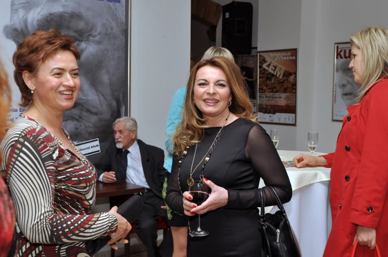 a woman standing next to a woman with a glass of wine