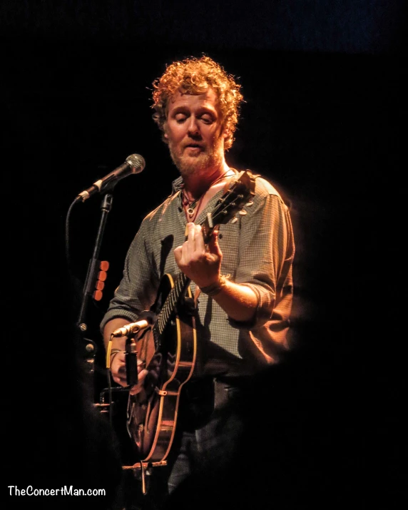 a person with an acoustic guitar standing near a microphone