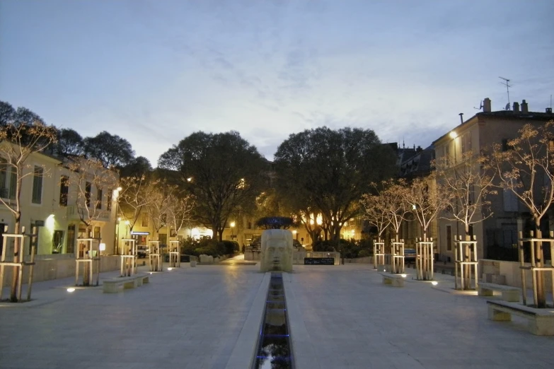 an empty walkway with lights surrounding and houses in the background