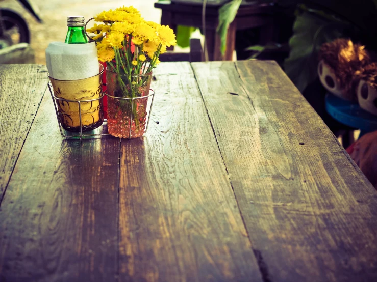 a vase of yellow flowers and a beer sit on a table