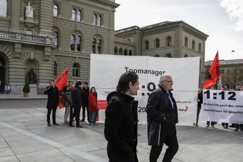 two men standing on a sidewalk and one has his hand out with protest signs