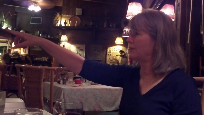 a woman sitting at a table pointing to her left