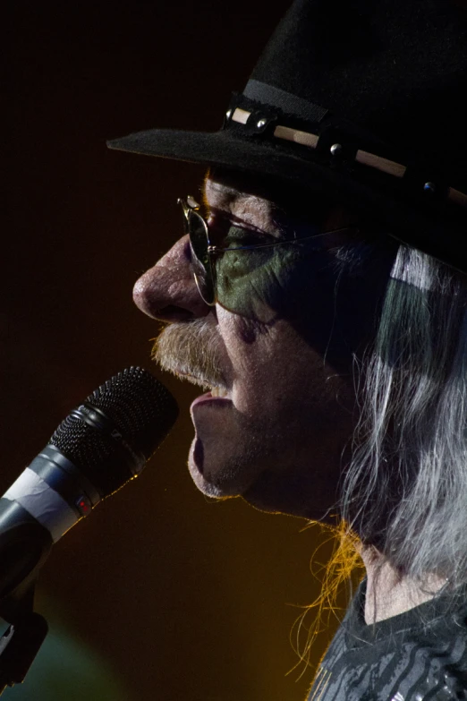 an old man with white hair and a long gray wig singing into a microphone