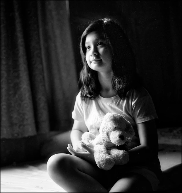 the girl sits on the floor holding a stuffed bear