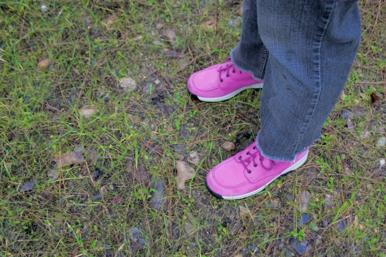 the feet of someone wearing pink tennis shoes on the grass