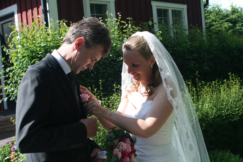 a man placing flower on his dress while the woman is holding it