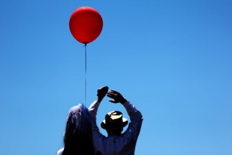 a man with his head turned away holding a red balloon