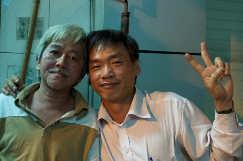 two asian men posing together, one man is holding a peace sign