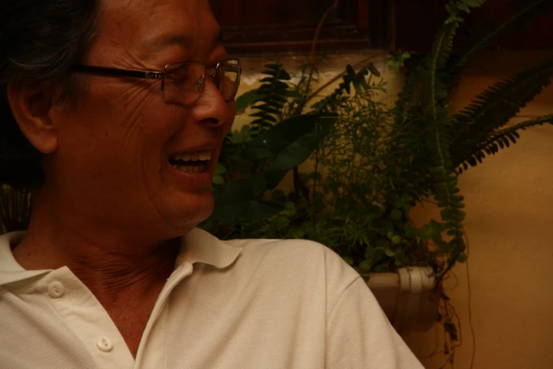 an old asian man smiling while sitting in front of some plants