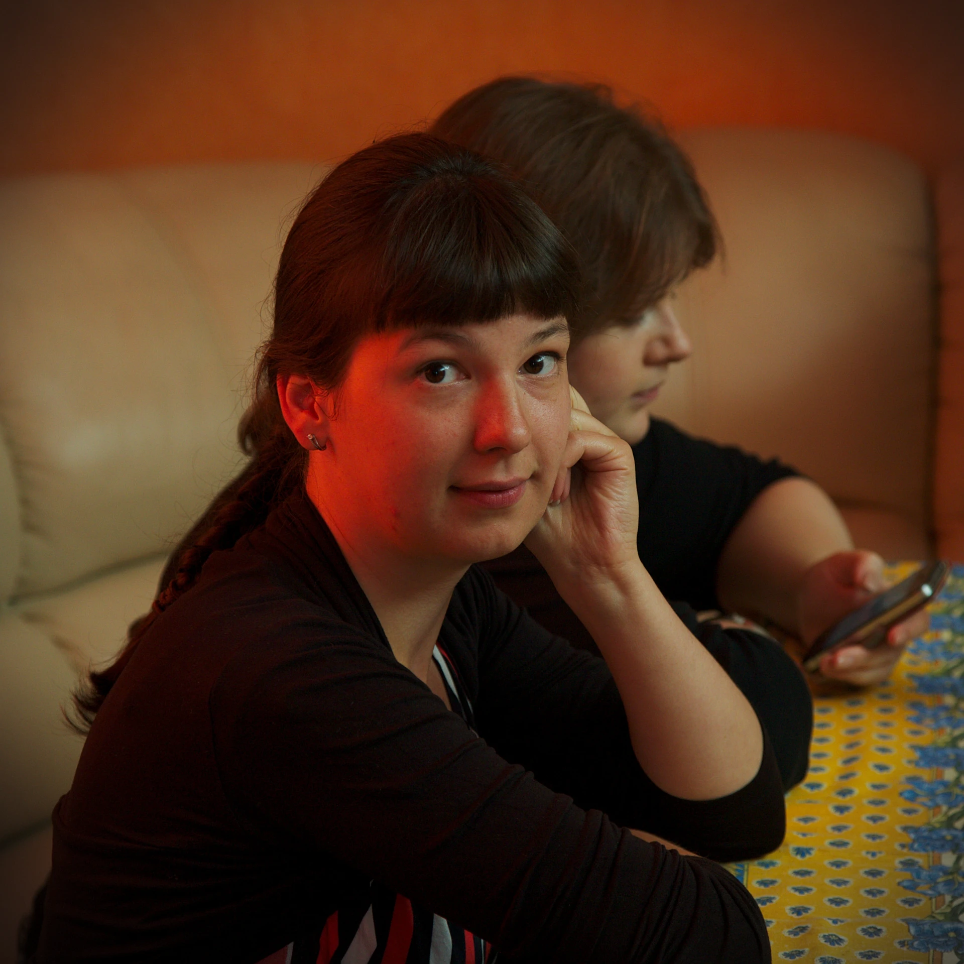 two young ladies sitting at a table and holding remote controls