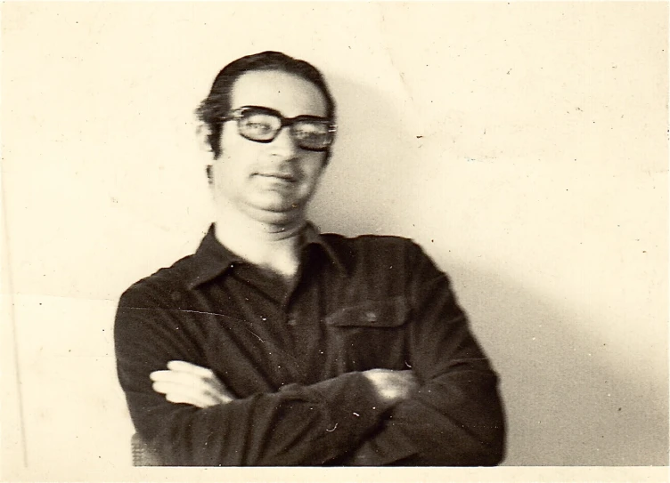 man in glasses leaning against white wall with folded arms