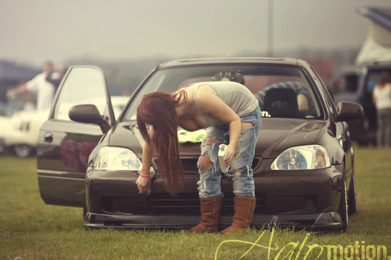 a woman bending down on her car in a field