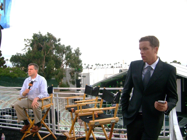 two men in business attire sitting on wooden chairs