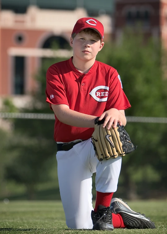 a little boy in red and white baseball uniform holding a glove