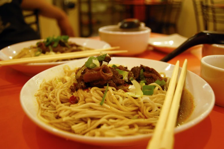 a plate full of noodles and meat in chopsticks