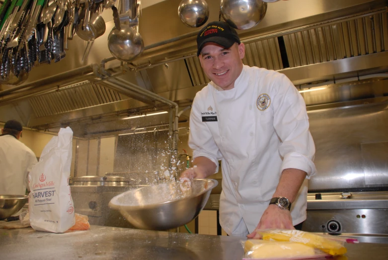 a chef in a kitchen is sprinkling his food with a large metal bowl