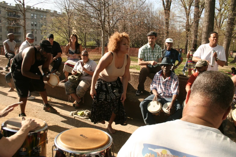 a woman is standing next to a group of people, who are holding drums