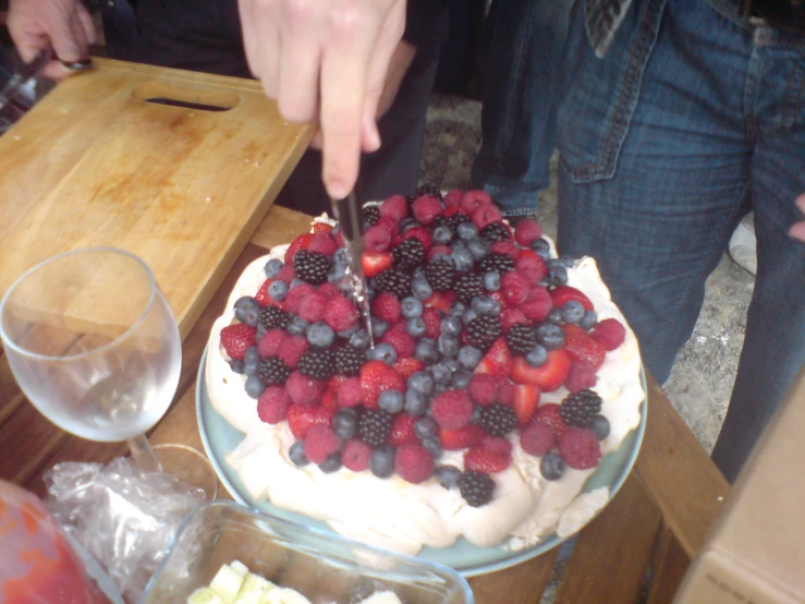 a person slicing a berry covered cake with a knife